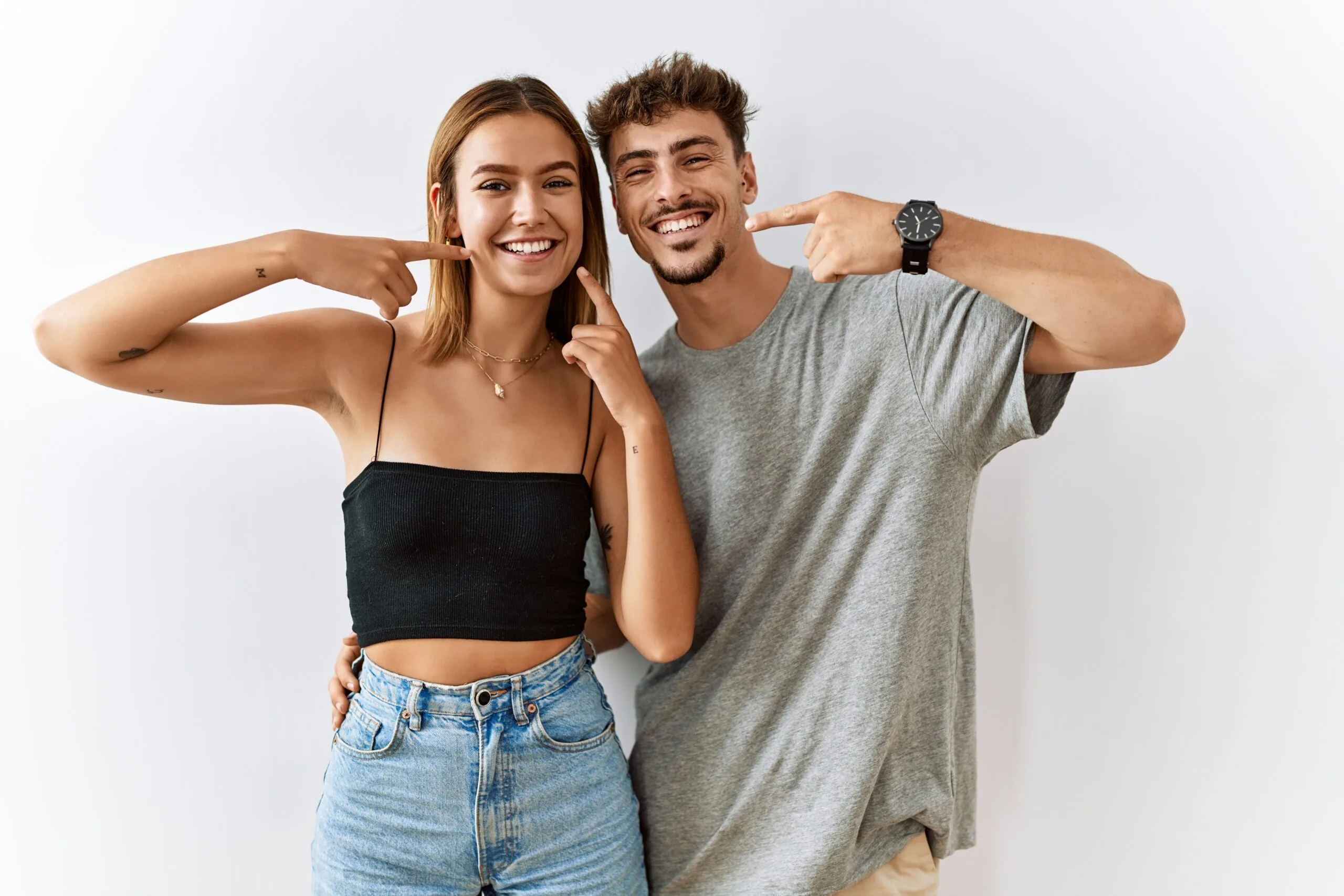 two confident young adults pointing to their perfect smiles